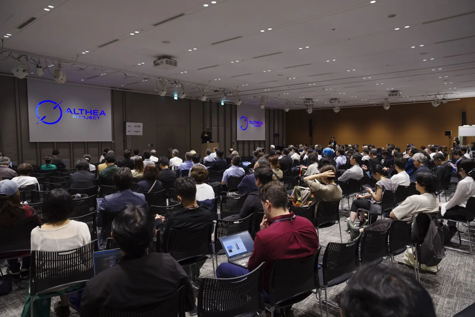 満席の会場。中央のスクリーンの前で登壇者が語る