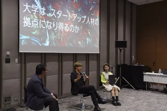 「大学は、スタートアップ人材の拠点になり得るのか」のスクリーンの前で語り合う3人の登壇者