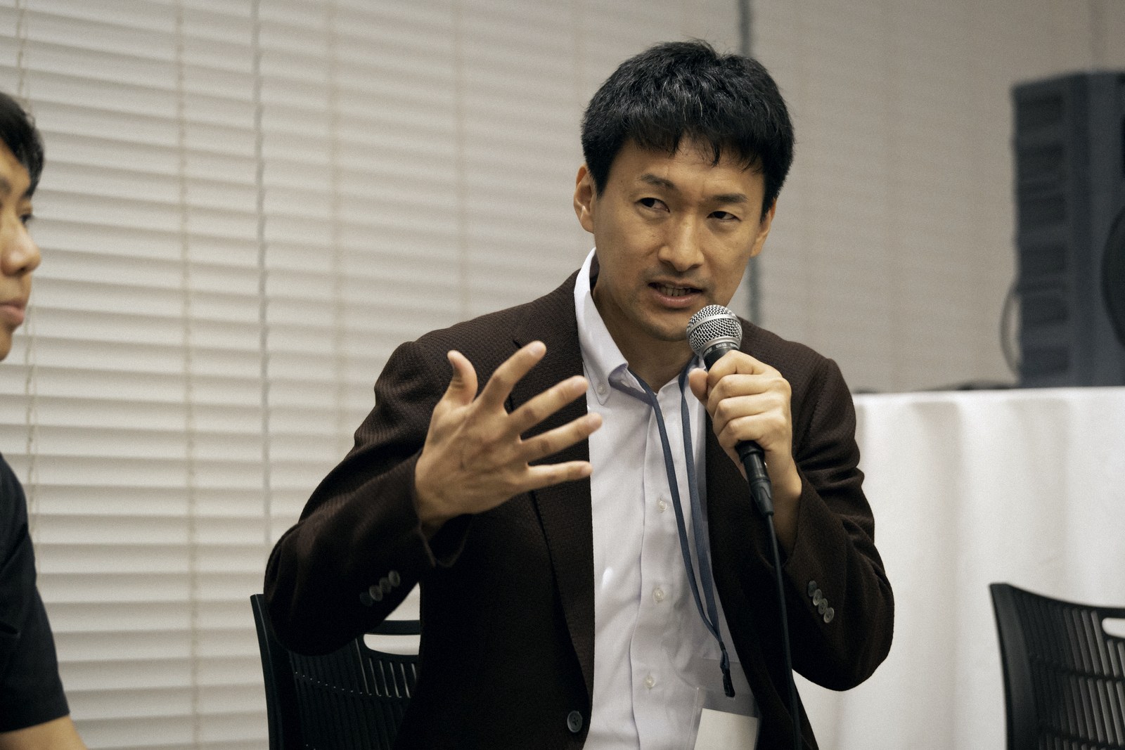 A speaker in a brown jacket speaking passionately with gestures